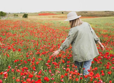 A girl in a summer hat walks through a blooming poppy field in summer. Nature pastime theme.