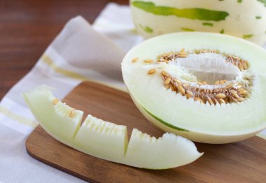 Yarım olgun kavun ve dilimlenmiş bir parça masanın üzerindeki tahta kesme tahtasının üzerinde..