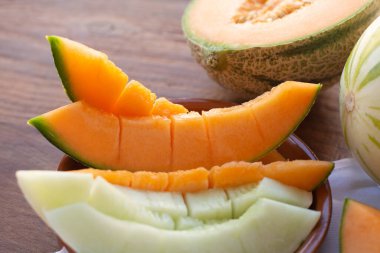 Çizgili kavun ve kavun parçalanmış bir tabakta, ahşap bir masanın arka planında yatıyor.. 