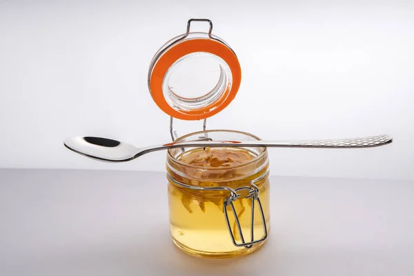 Homemade syrup of quince in glass jar with the spoon lying above on a white and grey background with free copy space
