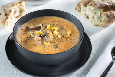 Krem peynir çorbası, mantarlı ve patatesli. Beyaz masada siyah kâse içinde leziz bir ilk yemek. Üst görünüm yatay.