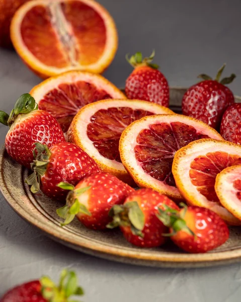 Gri arka planda dilimlenmiş kırmızı turuncu ve çilekli meyve tabağı, vitamin meyveleri konsepti, seçici odak