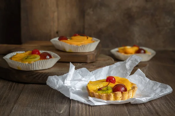 Beyaz kağıda meyveli ve kirazlı dört jöleli tart ve kahverengi ahşap arka plan.