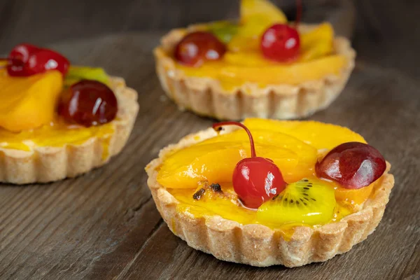 Kahverengi ahşap arka planda meyveli ve kirazlı üç jöleli tart.