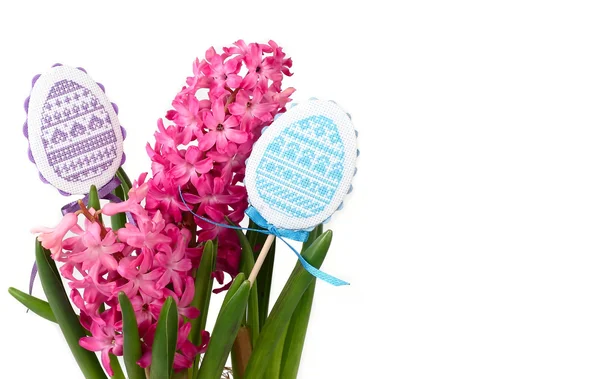 Roze hyacinten en de decoratieve geborduurde eieren op stokjes op een witte achtergrond. Een achtergrond van Pasen met de plaats van de tekst. — Stockfoto