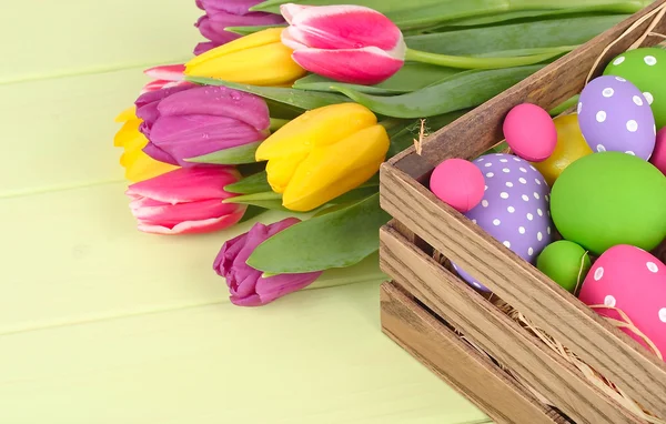 Heldere paaseieren van verschillende bloemen en lente tulpen op een groene houten achtergrond. Een achtergrond van Pasen met ruimte voor de tekst. — Stockfoto
