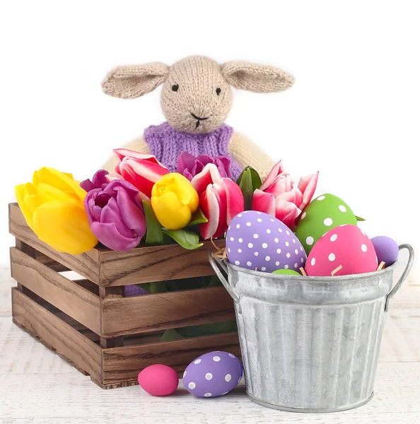 Tulipas em uma caixa de madeira, ovos de Páscoa e um coelho tricotado em um fundo branco. Um fundo de Páscoa com espaço para o texto . — Fotografia de Stock