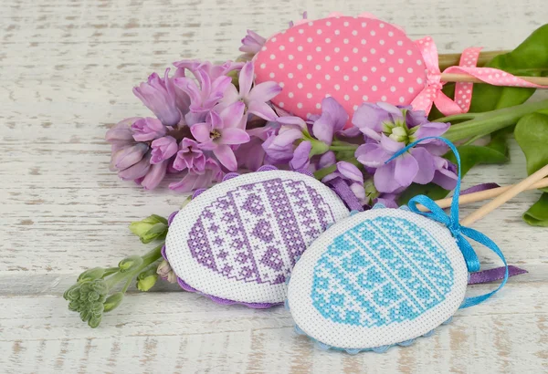 The Easter decorative embroidered eggs on sticks and a violet flower on a light wooden background. — Stock Photo, Image