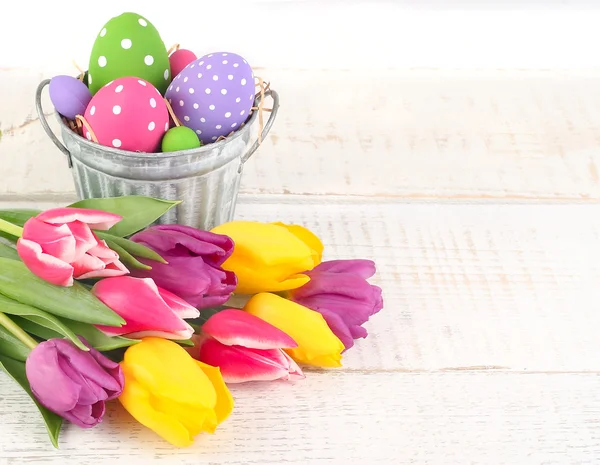 Huevos de Pascua en un cubo y brillantes tulipanes de primavera sobre un fondo de madera clara. Un fondo de Pascua con espacio para el texto. Formato vertical . —  Fotos de Stock