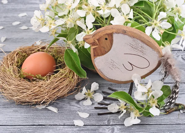 Paas-ei in een nest, een vogeltje en de bloeiende takken van het voorjaar op een houten grijze achtergrond. Een achtergrond van Pasen met ruimte voor de tekst. — Stockfoto