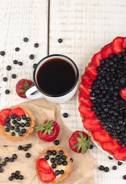Sommer-Mürbeteig mit Heidelbeere und Erdbeere und einer Tasse Schwarztee auf weißem Holzgrund. — Stockfoto