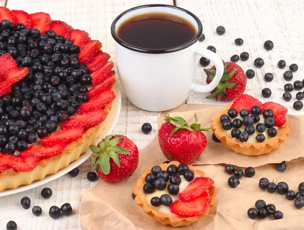 Sommerbeerenkuchen aus Shortcake-Teig und einer Tasse Schwarztee auf weißem Holzgrund. — Stockfoto