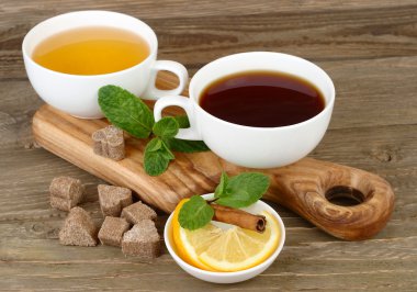 Two cups of black and green tea with a lemon, cinnamon and mint on a board on a wooden background. clipart