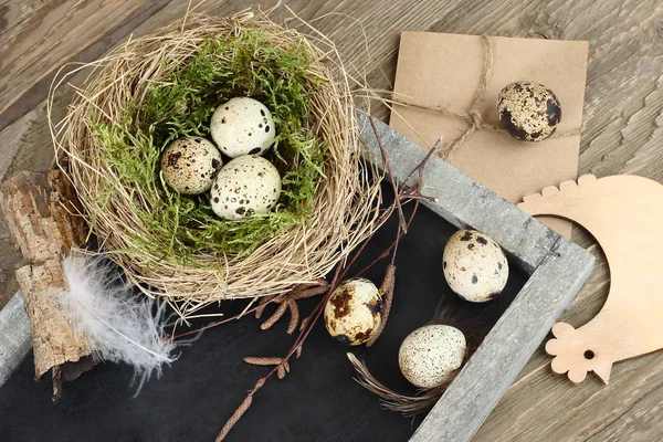 Easter eggs in nests and feathers on a blackboard on a wooden background. Easter background. — Stock Photo, Image