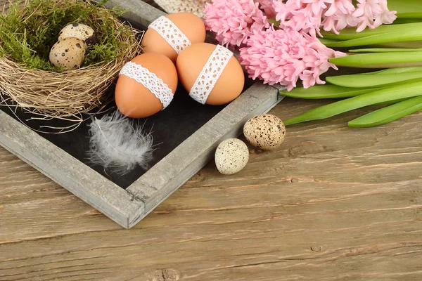 Pasen eieren op een schoolbord, een nest en hyacinten op een houten achtergrond. Pasen achtergrond. — Stockfoto