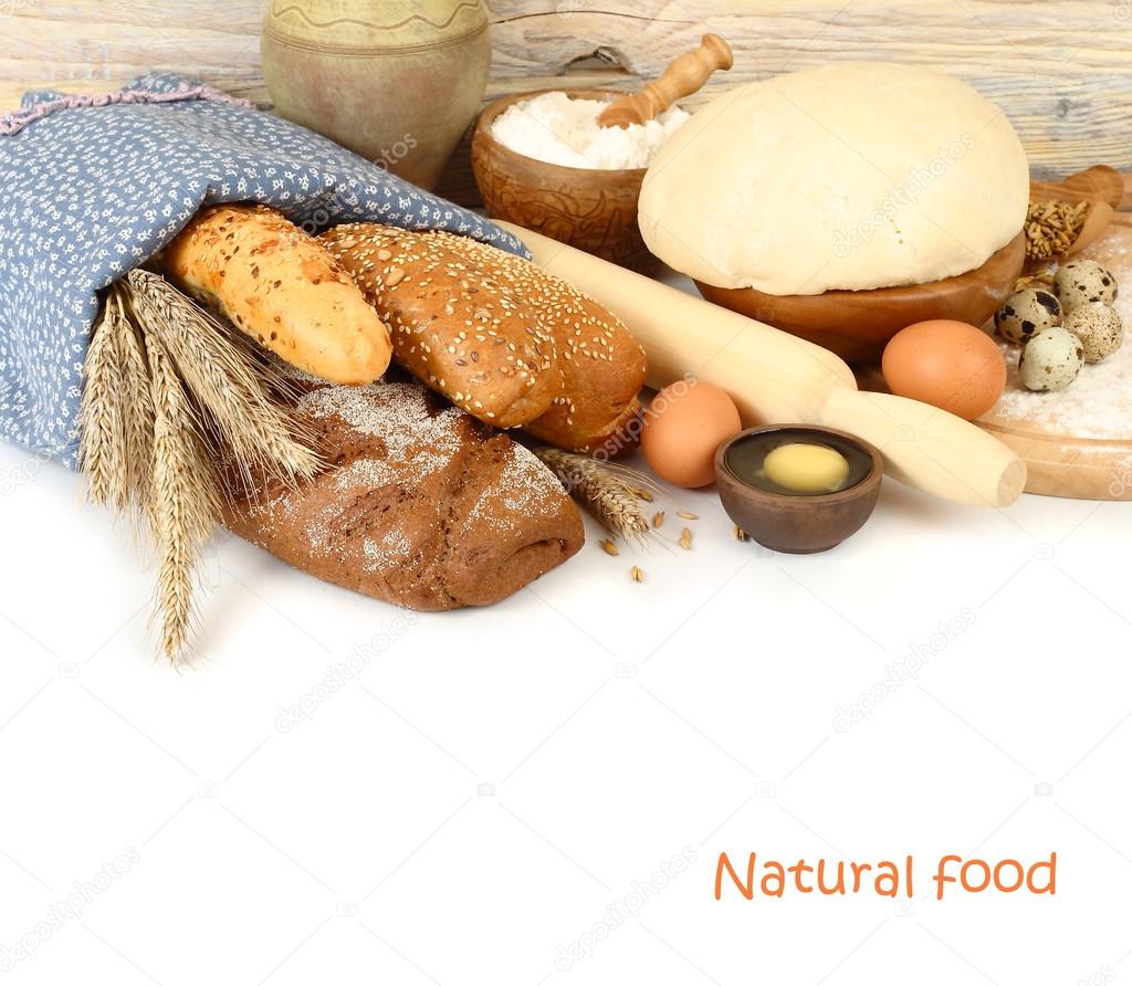Fresh fragrant bread under a linen napkin, dough and ingredients for baking of bread on a white background.