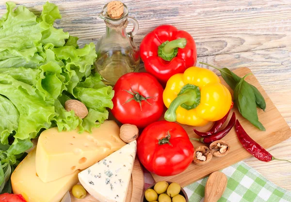 Kaas van verschillende rangen, verse groenten en olijven op een lichte houten achtergrond. Ingrediënten voor de voorbereiding van de Italiaanse Vegetarische pizza. — Stockfoto