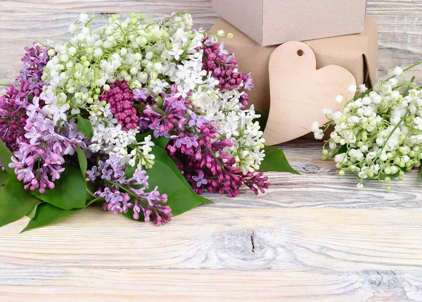 Okouzlující květy jarní šeřík a konvalinek a dárkové krabičky na dřevěné pozadí. Pozadí pro předmět "dovolenou" s prostorem pro text. — Stock fotografie