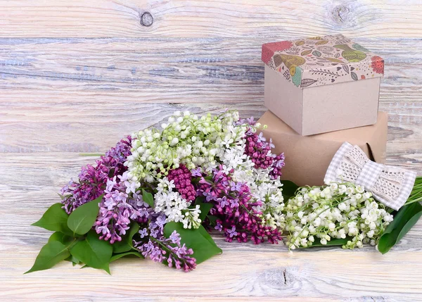 Boeketten van lelies van de vallei, een lila en geschenkdozen op een houten achtergrond. Een achtergrond voor het onderwerp "holiday". — Stockfoto