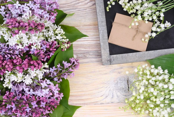 Fondo de flores con una lila, lirios del valle y un tablero cretácico con un lugar para el texto. Vista superior . — Foto de Stock