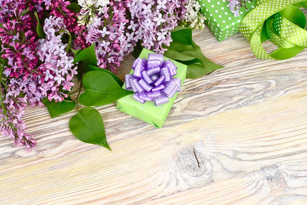 Flower wooden background with a lilac, a gift box and tapes with a place for the text. Top view. A background to the subject 