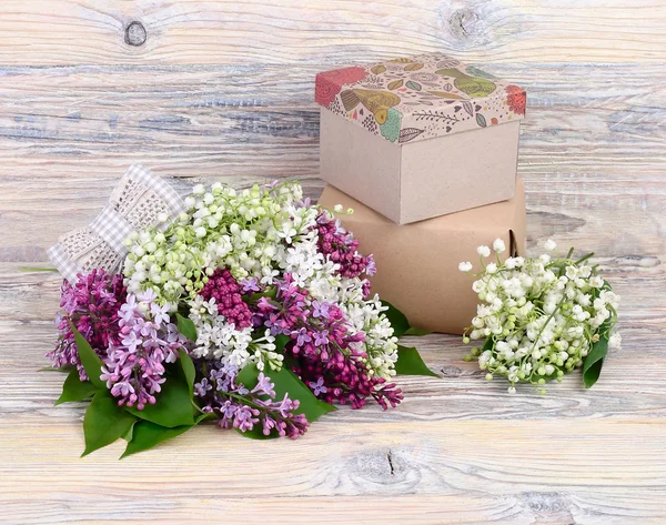 Fundo de madeira flor com um lilás, lírios do vale e caixas de presente com um lugar para o texto . — Fotografia de Stock