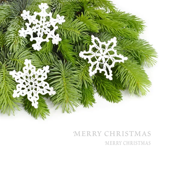 Bolyhos ága egy karácsonyfa, és a fehér háttér előtt kötött fehér hópelyhek. A karácsonyi háttér a hely, a szöveg. — Stock Fotó