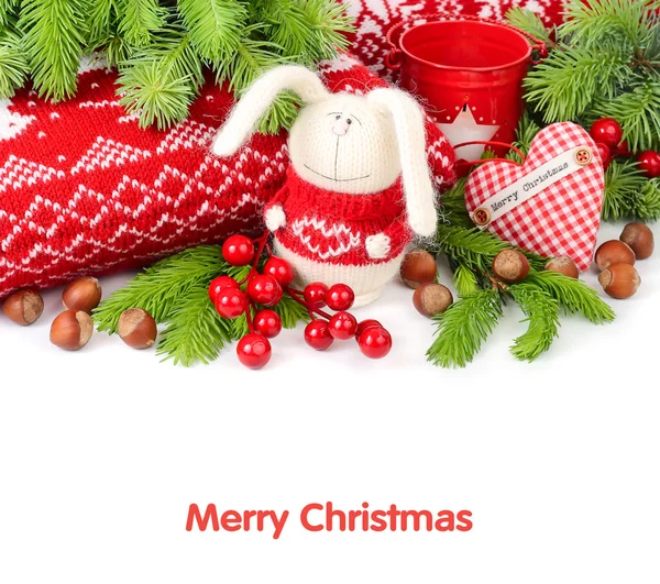 Gebreide haas, met textiel geruite hart, noten en kaneel in de buurt van gebreide kussens en takken van een kerstboom op een witte achtergrond. Kerst achtergrond. Rechtenvrije Stockfoto's