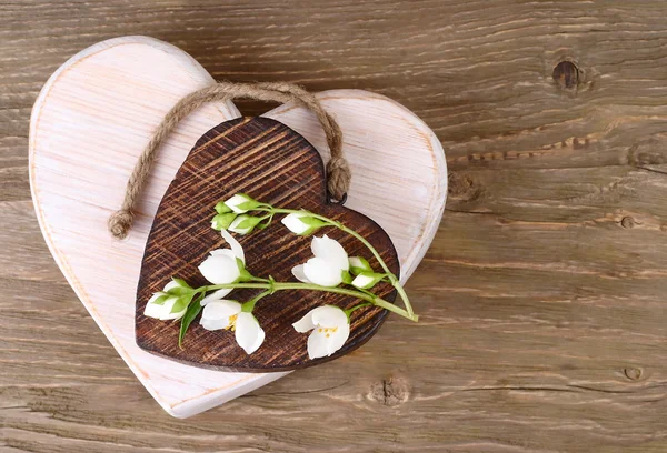 Dos corazones de madera y una rama de jazmín sobre un fondo de madera. Un trasfondo para el tema "amor". Vista superior . — Foto de Stock