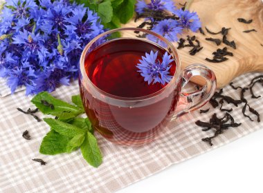 Transparent glass cup of black tea with mint and cornflowers on a white background. clipart