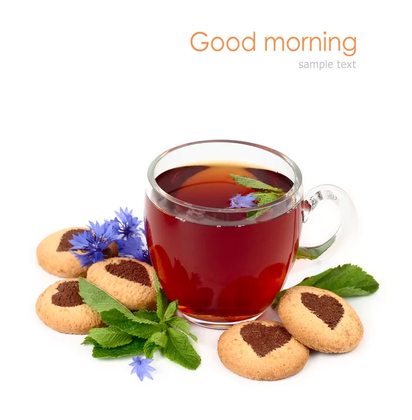 Transparent glass cup of black tea with mint and cornflowers and round shortcake with hearts on a white background. — 图库照片