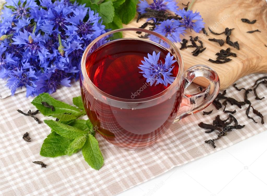 Transparent glass cup of black tea with mint and cornflowers on a white background.
