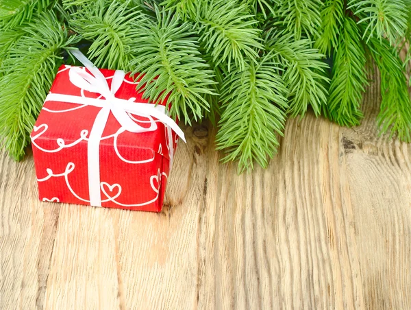 Scatola regalo rossa e rami morbidi di un albero di Natale su uno sfondo di legno chiaro. Uno sfondo natalizio con un posto per il testo . — Foto Stock