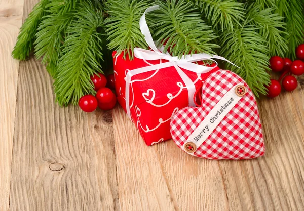 Red gift box and red checkered heart on branches of a Christmas tree on a wooden background. A Christmas background with a place for the text. — Stock Photo, Image