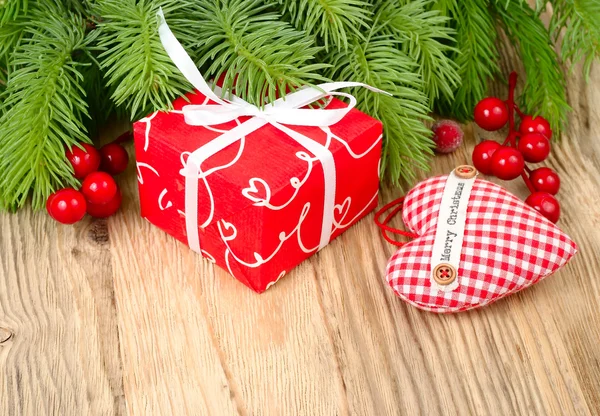 Caja de regalo roja y corazón rojo a cuadros en las ramas de un árbol de Navidad sobre un fondo de madera. Un fondo navideño con un lugar para el texto . —  Fotos de Stock