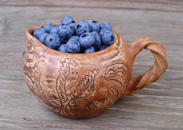 Fresh blueberry in a clay small jug on a wooden background. — Stock Photo, Image