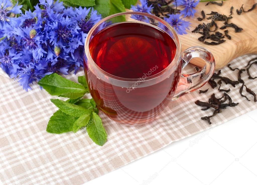 Cup of black tea with mint and cornflowers on a linen napkin on a white background.