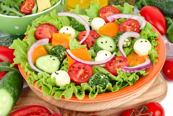 Der griechische Salat mit Käsebällchen auf einem orangefarbenen Teller auf einer rotkarierten Serviette und frischem reifem Gemüse und Kräutern auf weißem Hintergrund mit einem Platz für den Text. — Stockfoto