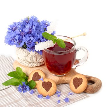 Black tea in a transparent mug with cornflowers and mint and cookies in the form of heart on a white background. clipart