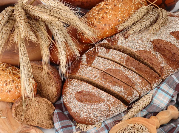 Pane fresco, grano e orecchie su un tovagliolo a scacchi su uno sfondo bianco con un posto per il testo . — Foto Stock