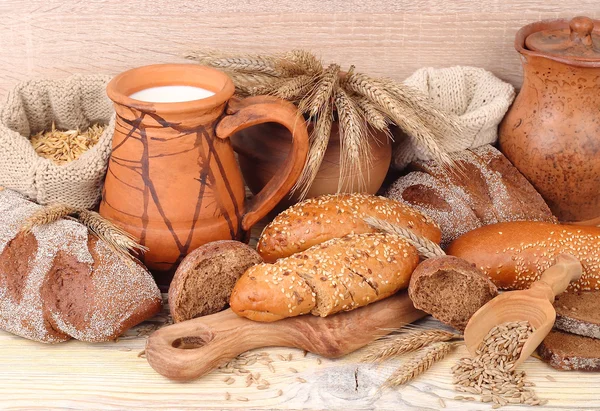 Pan fresco, espigas, granos y leche en una jarra sobre un fondo de madera . — Foto de Stock