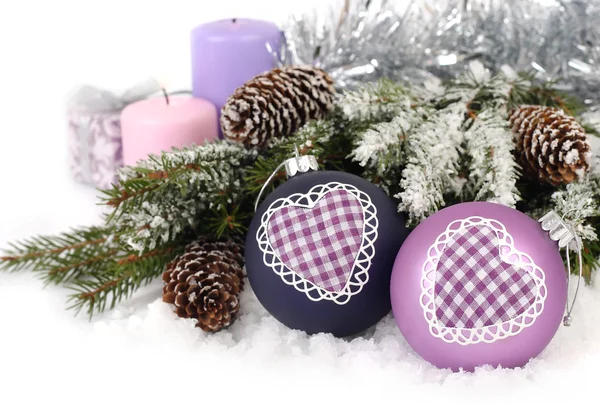 Bolas de Natal violetas com coração, cones e velas perto de ramos cobertos de neve de uma árvore de Natal em um contexto branco. Um fundo de Natal com um lugar para o texto . — Fotografia de Stock