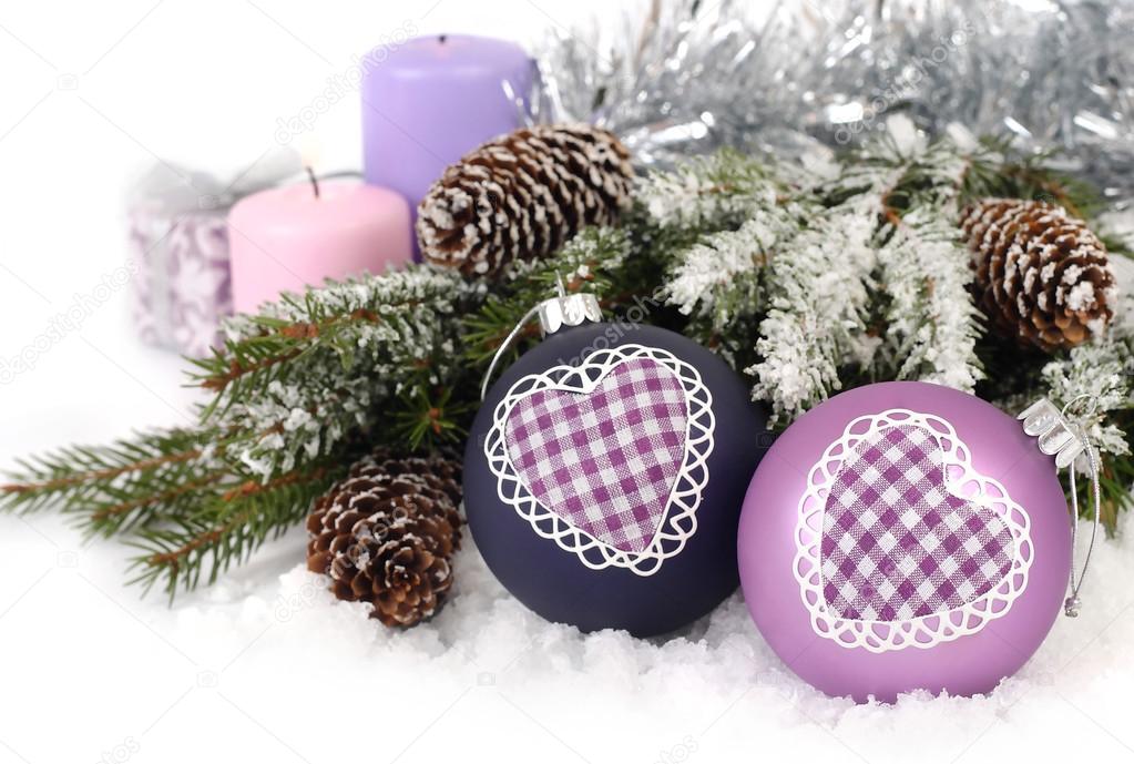 Violet Christmas balls with heart, cones and candles near snow-covered branches of a Christmas tree on a white background. A Christmas background with a place for the text.