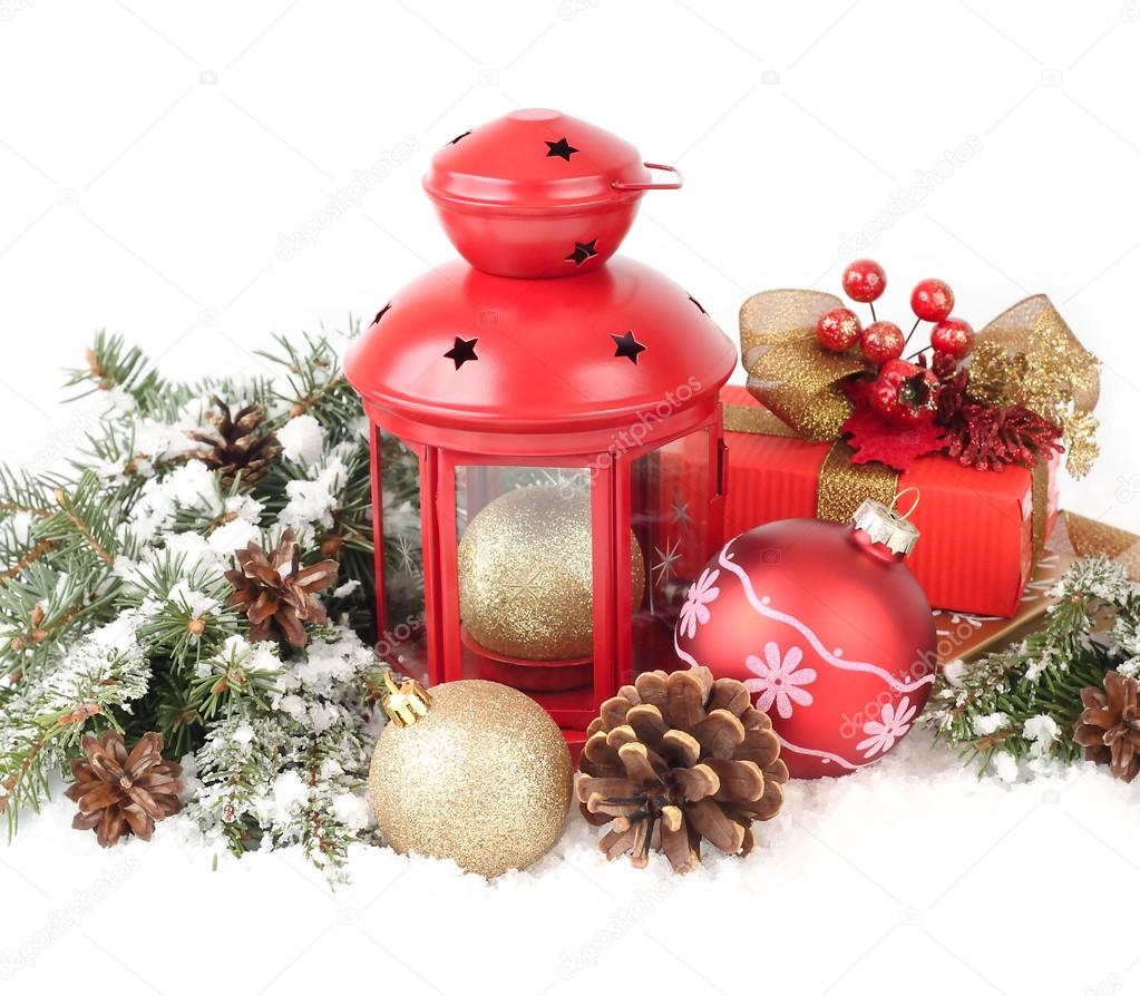 Christmas composition with a red small lamp candlestick and golden and red Christmas balls on snow-covered branches of a Christmas tree on a white background. A Christmas background with a place for the text.