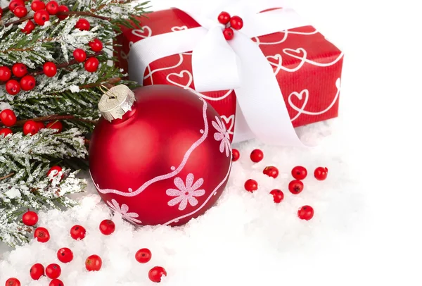 Bir kırmızı hediye kutusu ve karla kaplı beyaz zemin üzerinde bir Noel ağacının dalları üzerinde kırmızı meyveler Noel kompozisyonu. Bir Noel arka plan metni için bir yer ile.