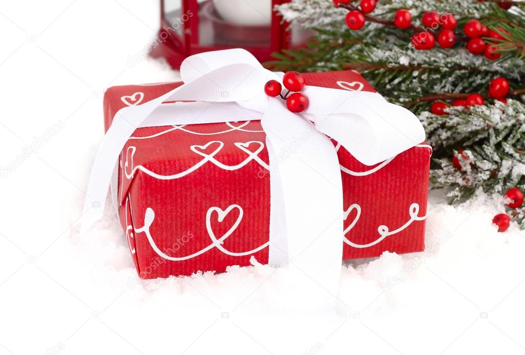 Christmas composition with a red gift box and red berries on snow-covered branches of a Christmas tree on a white background. A Christmas background with a place for the text.