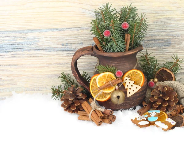 Χριστουγεννιάτικη σύνθεση με μια κανάτα με κλαδιά από ένα χριστουγεννιάτικο δέντρο, αποξηραμένα πορτοκάλια, κανέλα, καρύδια και πιπερόριζα μπισκότα στο χιόνι σε λευκό φόντο. Χριστούγεννα φόντο με μια θέση για το κείμενο. — Φωτογραφία Αρχείου