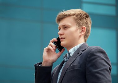 Modern bir binada yakınındaki bir smartphone cep telefonu ile konuşurken işadamı
