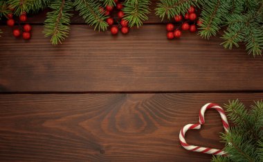 Noel Rustik tebrik kartı. Çam dalları, kırmızı böğürtlen, kahverengi ahşap arka planda kalp şeklinde noel lolipopları. Üst görünüm, metin için boşluk kopyala.