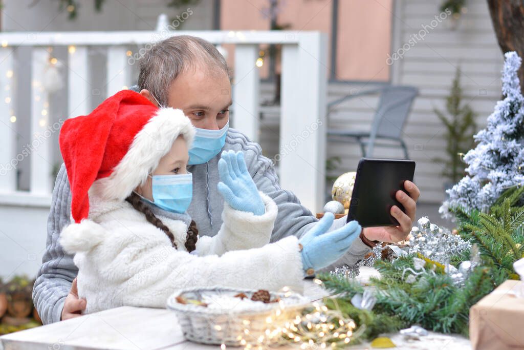 Dad and daughter in protective medical masks and a Santa hat wish Merry Christmas via messenger. Safe happy new year's and Merry christmasgreetings via messenger during quarantine covid 19 concept